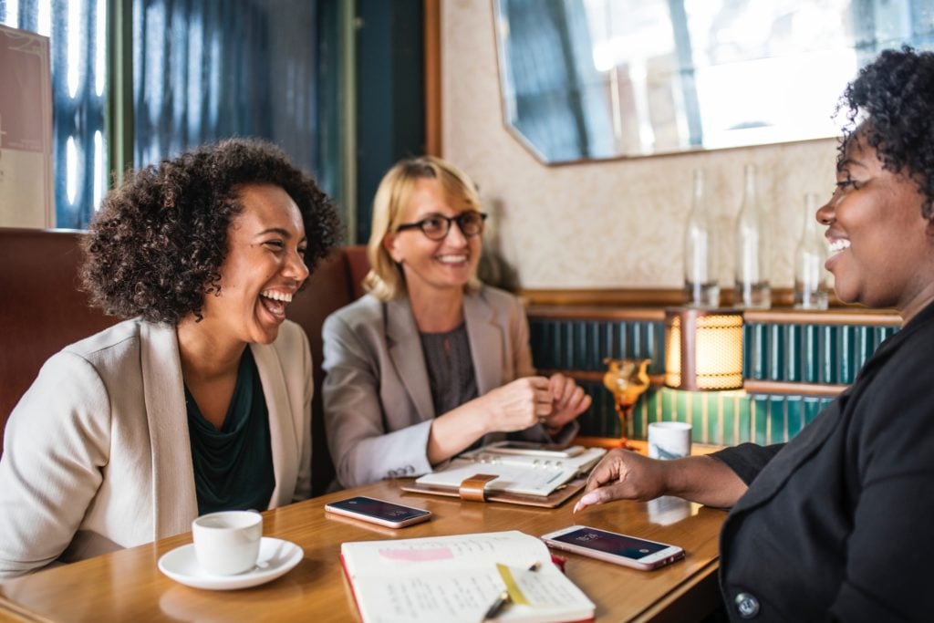 Three women having coffee and a business conversation at a diner - Search Influence