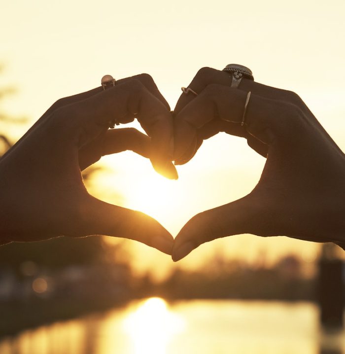 Two hands together making a heart with sun in background