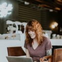 A redheaded woman sitting in a cafe working on a laptop