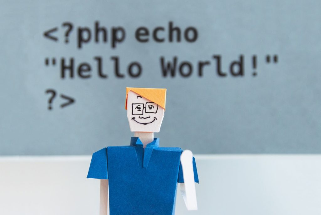 A paper man sitting in front of HTML code reading 'Hello World'