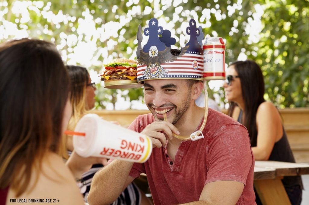 Man with Burger King hat with burger and Budweiser attached and woman drinking soda