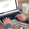 Person searching Google on a laptop at a desk with smarthpone