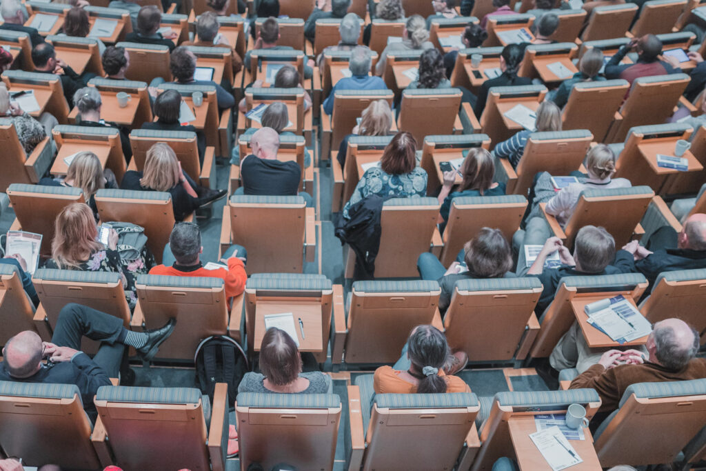 Large group of spectators watching a presentation in a lecture hall - Search Influence