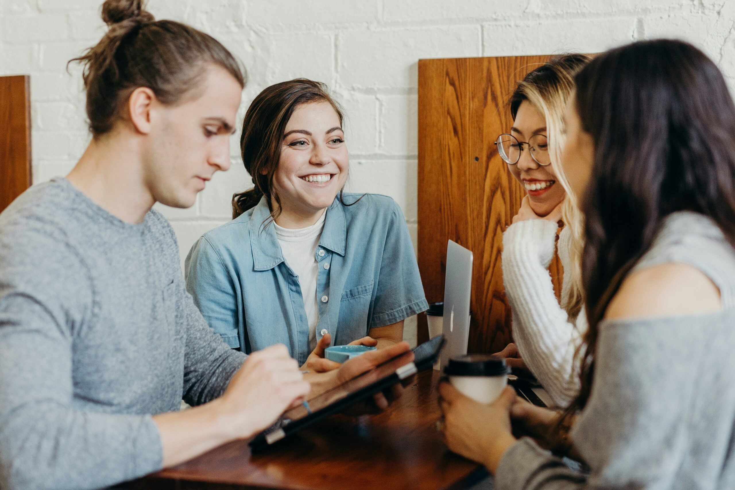 Four young adults chatting around a table with coffee and a tablet.