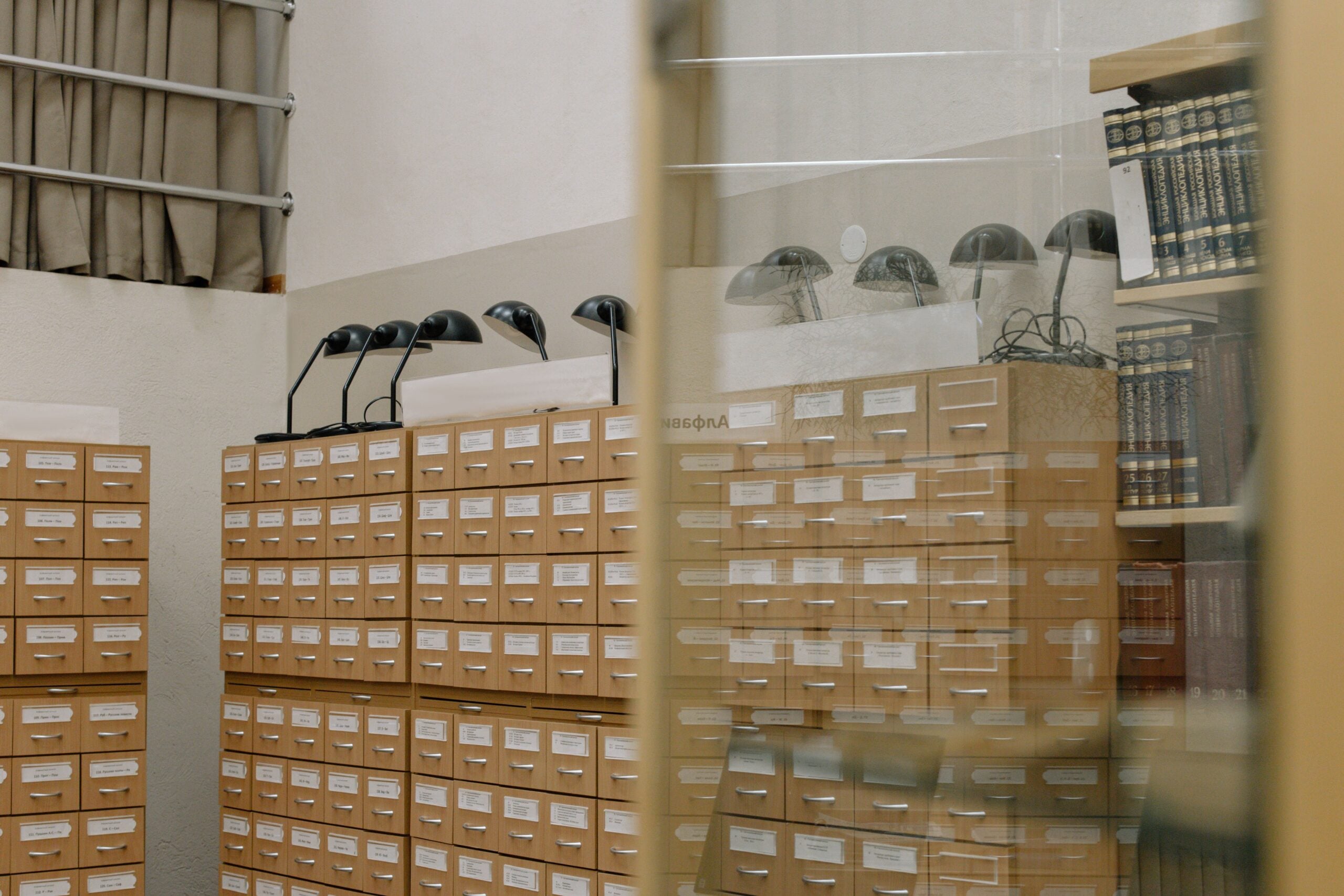Library card catalog drawers with reading lamps and bookshelves reflected in glass